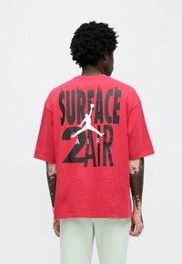 Κόκκινο υπερμεγέθες μπλουζάκι από βαμβάκι, με μεγάλο μαύρο κείμενο που γράφει "SURFACE 2 AIR" και λευκό σιλουέτα λογότυπο στην πλάτη.