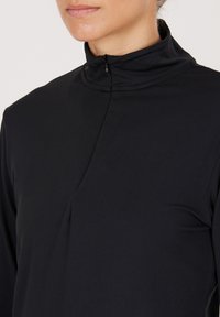 Black high-collar top with a half zipper, featuring a smooth texture and minimalistic design; includes a subtle pleat detail.