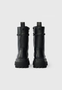 Melni ādas potīšu zābaki ar teksturētu virsmu, plakana gumijas zole un logotipam akcentēta cilpa. Iekļauts sānu ieejas rāvējslēdzis vieglai piekļuvei.