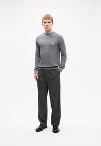 Cămașă gri texturată cu mânecă lungă, guler rotund și o mică patch, asociată cu pantaloni închiși la culoare cu un model și pantofi negri. Design simplu, modern.