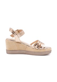 Złote metaliczne sandały na koturnie z wieloma krzyżującymi się paskami, teksturowana platforma espadrylowe oraz tylny pasek na kostkę dla wsparcia.