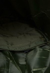 Olivno zeleno podloženo notranje območje s krožno obliko in gladko teksturo, vidnim zadrgo ob robu in brez dodatnih vzorcev.