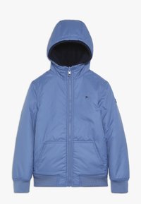 Jasnoniebieska pikowana kurtka z kapturem, z zamkiem błyskawicznym, elastycznymi mankietami i dwoma bocznymi kieszeniami. Miękka podszewka wewnętrzna.