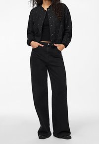 Svart bomberjacka med silverdetaljer, i kombination med en svart ribbad topp och breda svarta byxor. Materialet verkar slätt och texturerat.