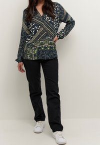 Langærmet, navyblå bluse med mønstre i blomster- og geometriske designs. Kombineret med sorte bukser og hvide sneakers, med v-halsudskæring.