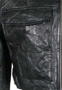 Schwarze Lederjacke mit strukturiertem Finish, auffälliger Tasche auf der Vorderseite und metallischem Reißverschluss als Verschluss.