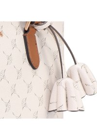 Borsa beige con motivo floreale in rilievo, dettagli in pelle e due nappine a forma di campana testurizzate. Presenta una maniglia in corda intrecciata.