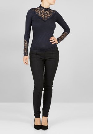 Marinblå ribbade långärmade topp med genomskinlig spets i halsringningen, med mönstrade spetstillägg och matchad med smala svarta byxor och svarta klackar.