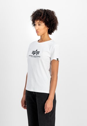 T-shirt en coton blanc avec un col rond, présentant un logo noir "Alpha Industries" et une petite étiquette de marque jaune sur la manche.