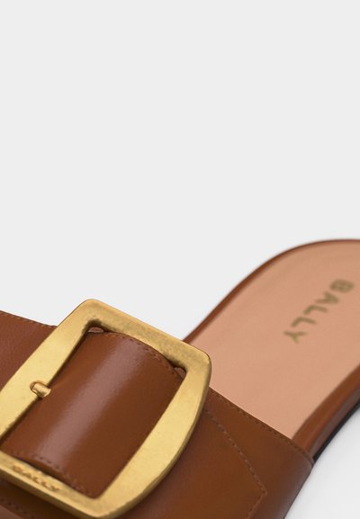 Sandale mule en cuir marron avec grande boucle dorée et semelle intérieure beige marquée "BALLY" sur fond blanc.