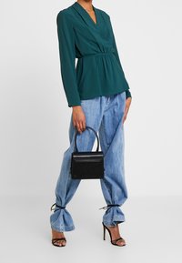 Grön texturerad blus med V-ringning och rynkad midja. Känns bra ihop med ljusblå baggy jeans, svarta klacksandaler och en liten svart handväska.