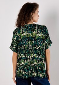 Kurzarmbluse in einem grünen, schwarzen und weißen abstrakten Muster. Weicher Stoff mit lockerer Passform und rundem Ausschnitt.