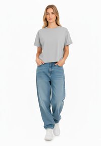 T-shirt grigio corto con maniche corte abbinato a jeans a gamba dritta a vita alta di colore blu chiaro e sneakers bianche.