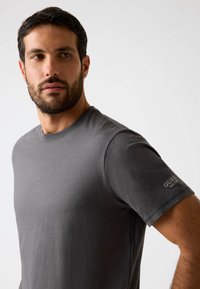 Graues Baumwoll-T-Shirt mit Rundhalsausschnitt, kurzen Ärmeln und einem dezenten Markenlogo am linken Ärmel. Glatte Textur und figurbetontes Design.