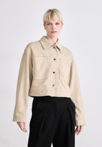 Bežna skrajšana denim jakna s konico ovratnika, sprednjimi žepi in črnimi gumbi. Gladka tekstura z strukturiranim prileganjem.