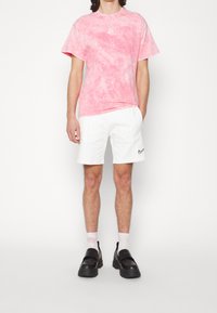 Pink tie-dye T-shirt, white athletic shorts, and black slip-on shoes. Soft fabric, relaxed fit, notable Nike logo on the shirt and shorts.