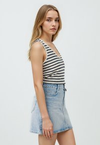Gestreepte, mouwloze tanktop in crème en marineblauw. Gepaard met een lichtblauwe denim minirok. Beide stukken hebben een casual snit en afwerking.