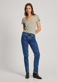 Zeleni stretch pamukasti T-shirt s V-izrezom, uparen s plavim trapericama visokog struka. Čizme do gležnja upotpunjuju odjevnu kombinaciju.