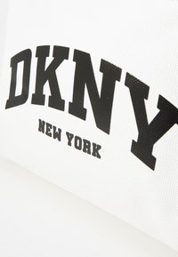 Borsa in tessuto bianco con il prominente logo nero "DKNY" e il testo "NEW YORK". Presenta una superficie testurizzata e un design con caratteri in grassetto.