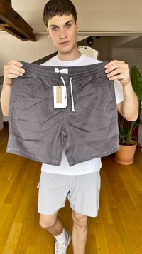 Gray shorts with an elastic waistband, drawstring, and two side pockets; made from soft, lightweight fabric. Tagged and held by a model.