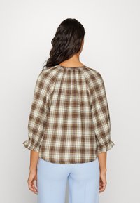 Brun och creamrutigt blus med en samlad halsringning och trekvartsärmar. Tyget är lättviktigt med en mjuk textur.