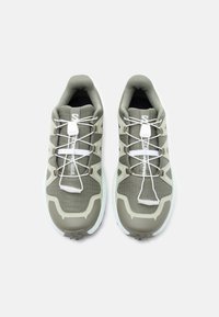 Par obu sivih in belih tekaških copat za steze s hitrim zateznim vezalkam, pogled iz zraka na preprostem belem ozadju.