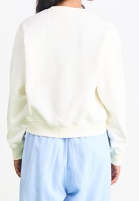 Krämsfärgad sweatshirt med rund halsringning, långa ärmar och ribbad fåll, tillsammans med ljusblå, löst sittande byxor.