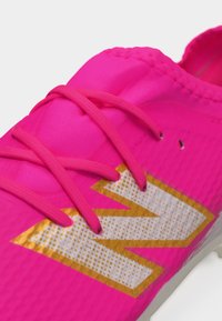 Chaussure de sport d'un rose vif avec des lacets assortis et un grand logo "N" blanc et or sur le côté.