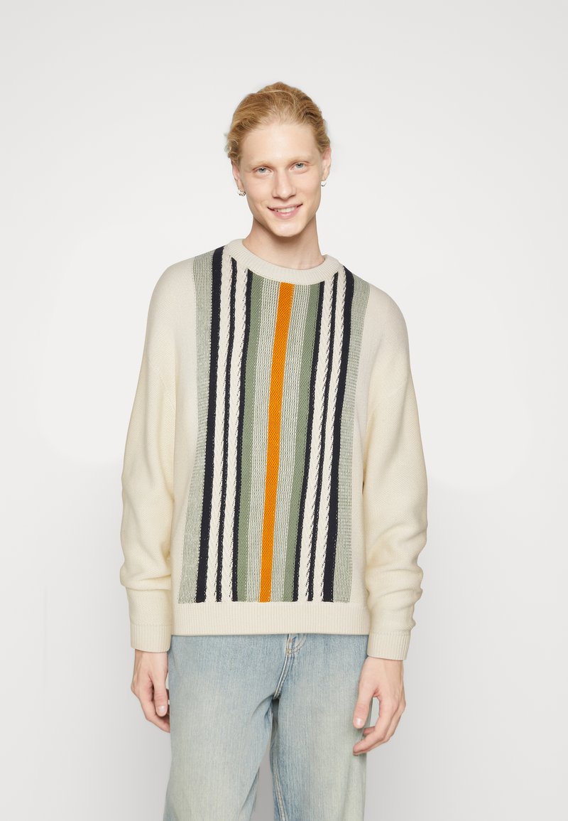 Pull en tricot crème avec des rayures verticales multicolores, y compris du vert, du bleu marine et de l'orange. Doté d'un col rond et d'une coupe décontractée.