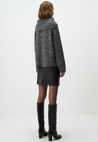 Veste en tricot grise avec un col montant, associée à une jupe en cuir noir et des bottes noires montantes, vue de dos.