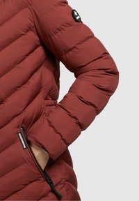 Chaqueta de plumas burdeos con un patrón de costura horizontal, que cuenta con un bolsillo con cremallera y un parche del logo en la manga. Textura de tela suave.