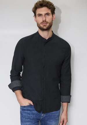 Camisa de botón en tela negra con cuello mandarina, mangas largas y acento gris en los puños vuelta. Textura suave, corte clásico.
