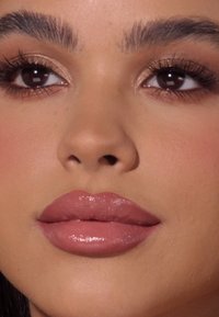 Primer plano de un rostro con labios lisos y llenos de un tono nude brillante, cejas bien arregladas y sombra de ojos sutil que resalta.