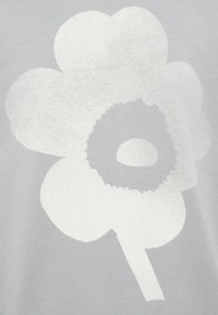 Camiseta gris con un gran diseño de flor blanca con pétalos redondeados y un centro circular. La textura es suave y la tela es blanda.