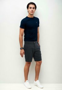 Navy blue fitted t-shirt, gray shorts with pockets, and white sneakers. Subtle logo on the t-shirt. Casual look with a sleek design.
