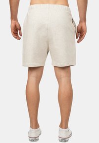 Pantaloni corti in cotone beige chiaro con vita elasticizzata, tasche laterali e vestibilità comoda, abbinati a sneakers bianche.