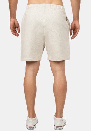 Shorts en mélange de coton beige clair avec une taille élastique, des poches latérales et une coupe décontractée, associés à des baskets blanches.