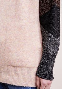 Stickad tröja med gradientdesign; mjuk rosa kropp med svarta ärmar med metalliska accenter. Ribbad fåll och texturerade variationer i tyget.