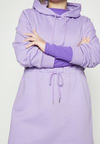 Robe sweat à capuche violet clair avec taille à cordon de serrage, manches longues et détails de poignets côtelés. Tissu doux avec une coupe décontractée.