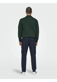 Felpa verde con colletto, pantaloni cargo blu navy con tasche laterali e sneakers bianche con accenti neri. Design semplice e casual.