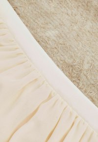 Tejido beige texturizado con una superficie esponjosa adyacente a un material liso de color rosa claro, presentando detalles fruncidos y un borde blanco.