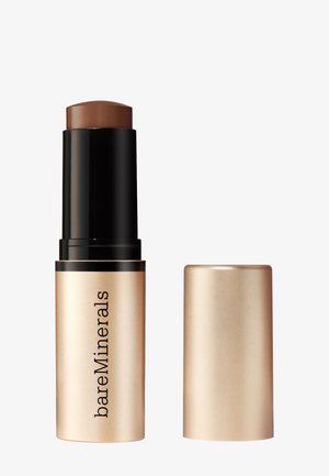 Fond de teint stick de teinte marron foncé dans un tube doré mat, étiqueté "bareMinerals", avec son bouchon assorti placé à côté.