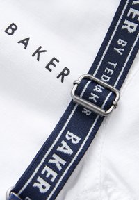 Biely textil s čiernym nápisom "BAKER". Námornícky pás s bielymi pruhmi a textom "BAKER by TED BAKER" zabezpečený striebornou prackou.