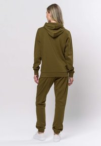 Set van olijfgroene hoodie en joggers gemaakt van zachte stof. De hoodie heeft een grote capuchon en geribbelde manchetten. De joggers zijn voorzien van elastische enkels.