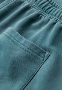 Shorts en coton teal avec une taille élastique, dotés d'une seule poche latérale et d'un tissu lisse et texturé.