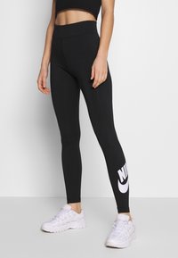Zwarte high-waisted legging van rekbaar materiaal, met een groot wit Nike-logo op de onderste linkerpijp en een gladde, stijlvolle uitstraling.