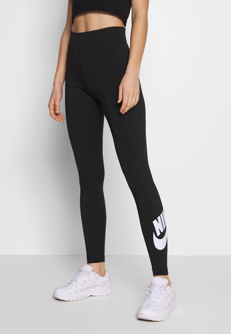 Zwarte high-waisted legging van rekbaar materiaal, met een groot wit Nike-logo op de onderste linkerpijp en een gladde, stijlvolle uitstraling.