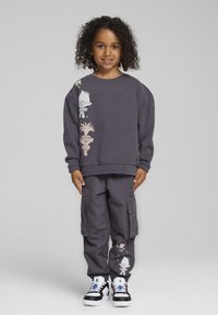 Un sudadera gris y pantalones cargo presentan gráficos de personajes de dibujos animados. El conjunto tiene un corte holgado y se complementa con zapatillas negras y blancas.