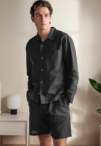 Black linen short-sleeve shirt with front pocket and buttons, paired with matching shorts. Smooth texture, casual fit.