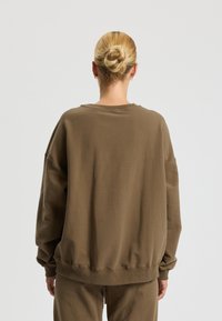 Brown cotton sweatshirt with a relaxed fit, ribbed neckline and cuffs. Smooth texture, oversized sleeves, waistband sitting at the hip.